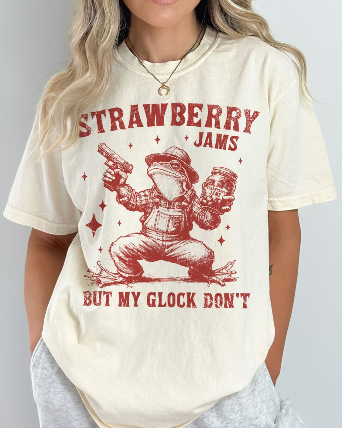 Woman wearing a natural Strawberry Jams But My Glock Don't Shirt with vintage cowboy frog graphic