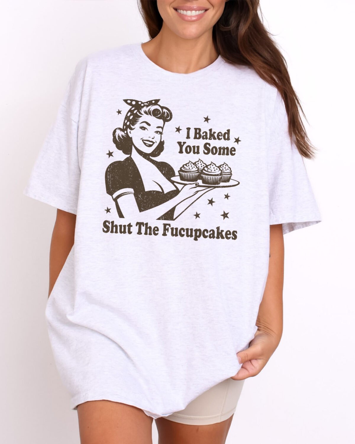 Woman wearing a funny quote "I Baked You Some Shut The Fucupcakes" Shirt in ash grey color with a vintage distressed housewife graphic