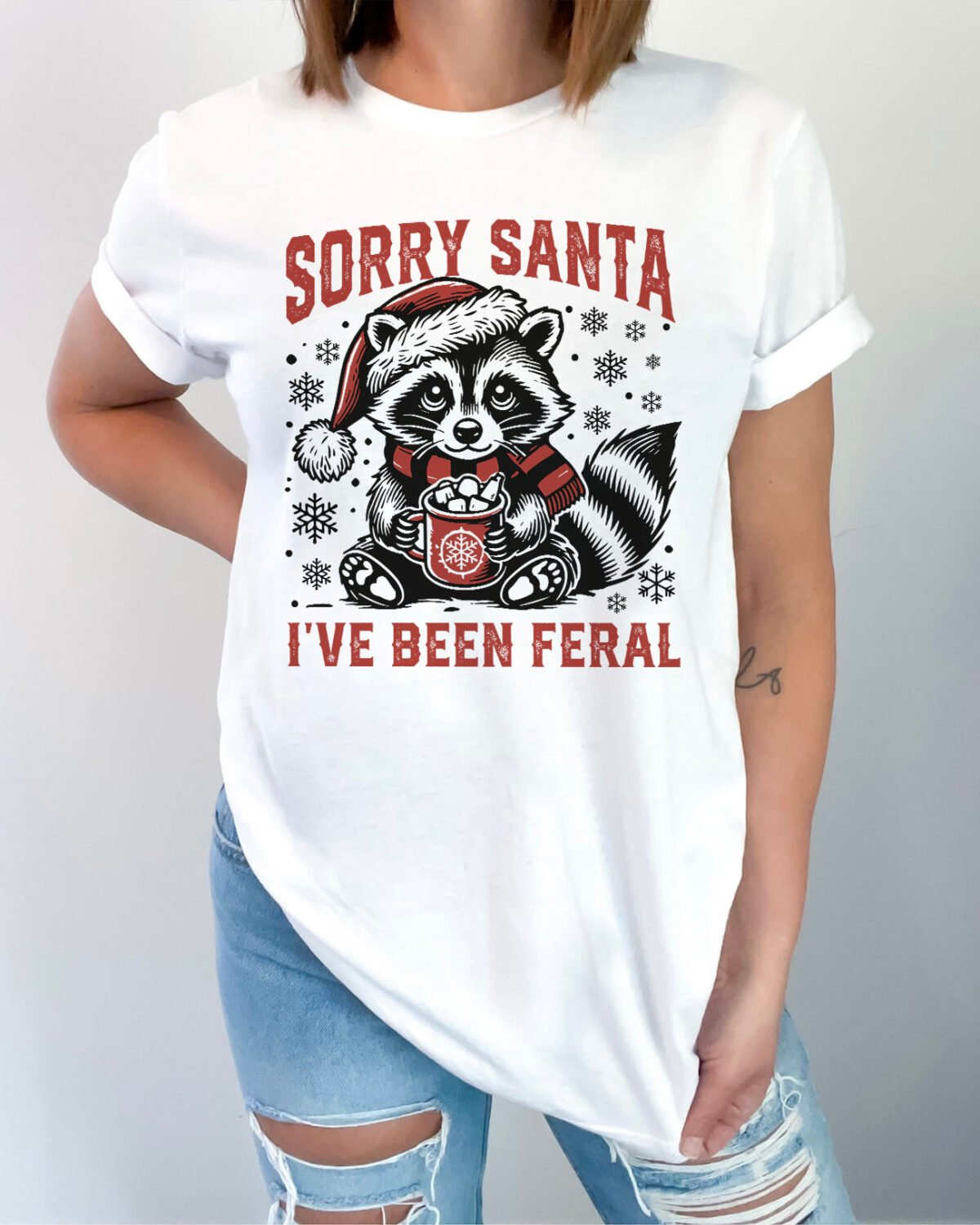 Woman wearing a Sorry Santa I've Been Feral shirt in white color featuring a cute raccoon christmas graphic on the front